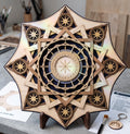 A multi-layered laser-cut wooden mandala art piece stands on a small wooden easel on a table with a paintbrush and layer guide nearby.