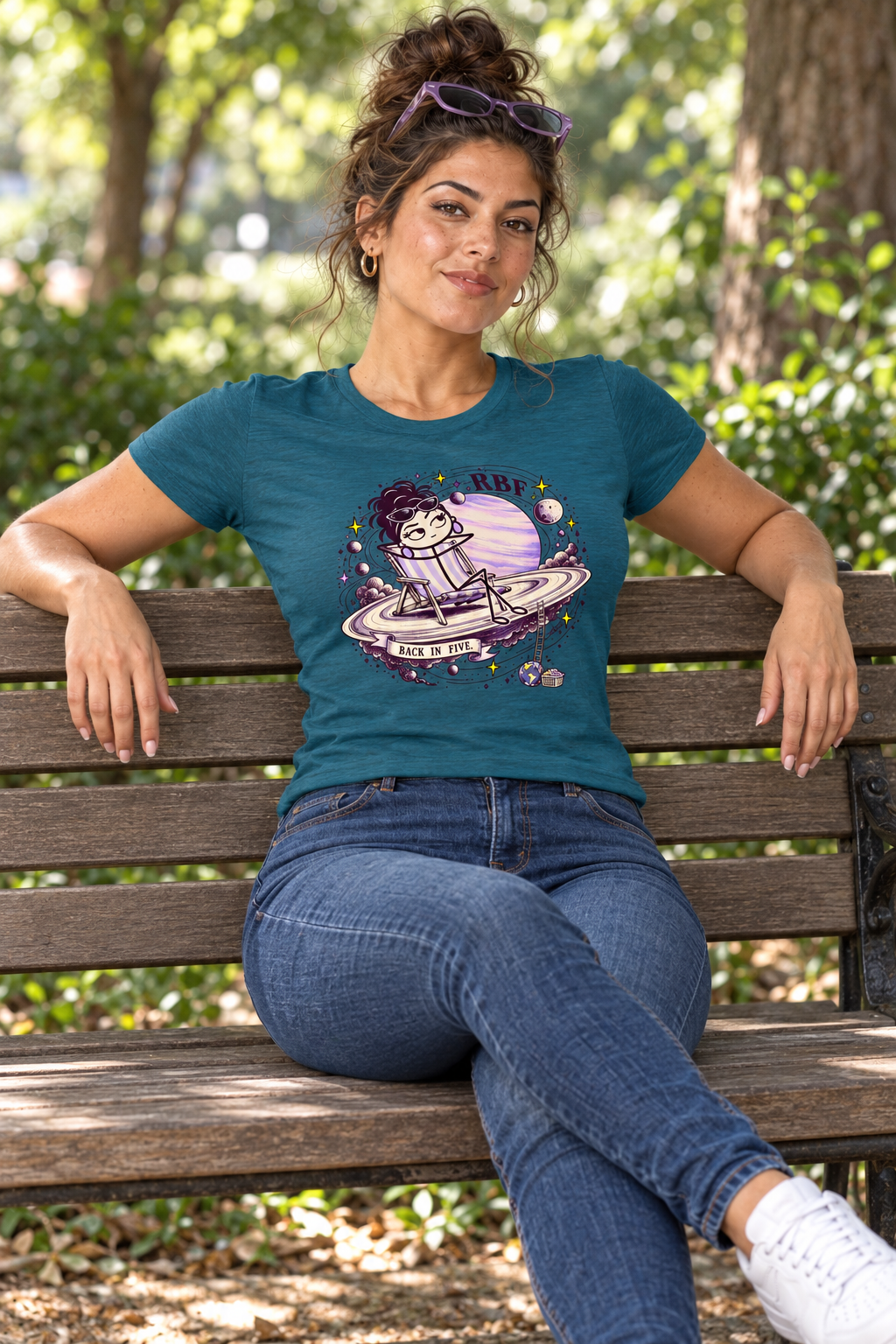 Lifestyle mockup: Back in Five graphic tee in Antique Sapphire. Seated on a park bench with the front design visible.