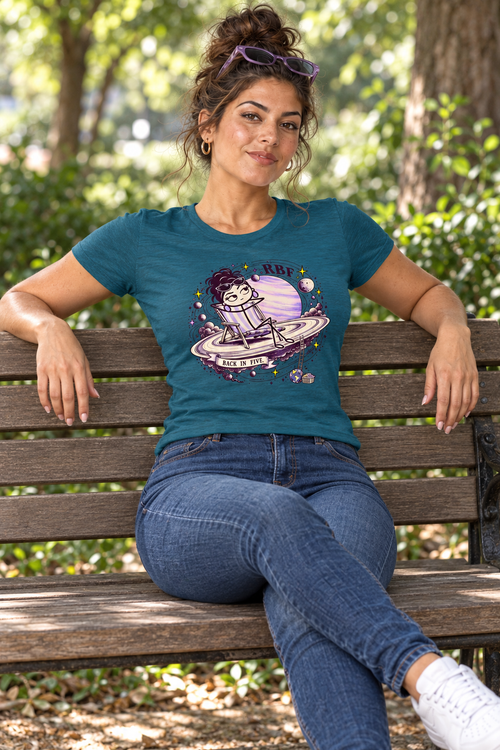 Lifestyle mockup: Back in Five graphic tee in Antique Sapphire. Seated on a park bench with the front design visible.