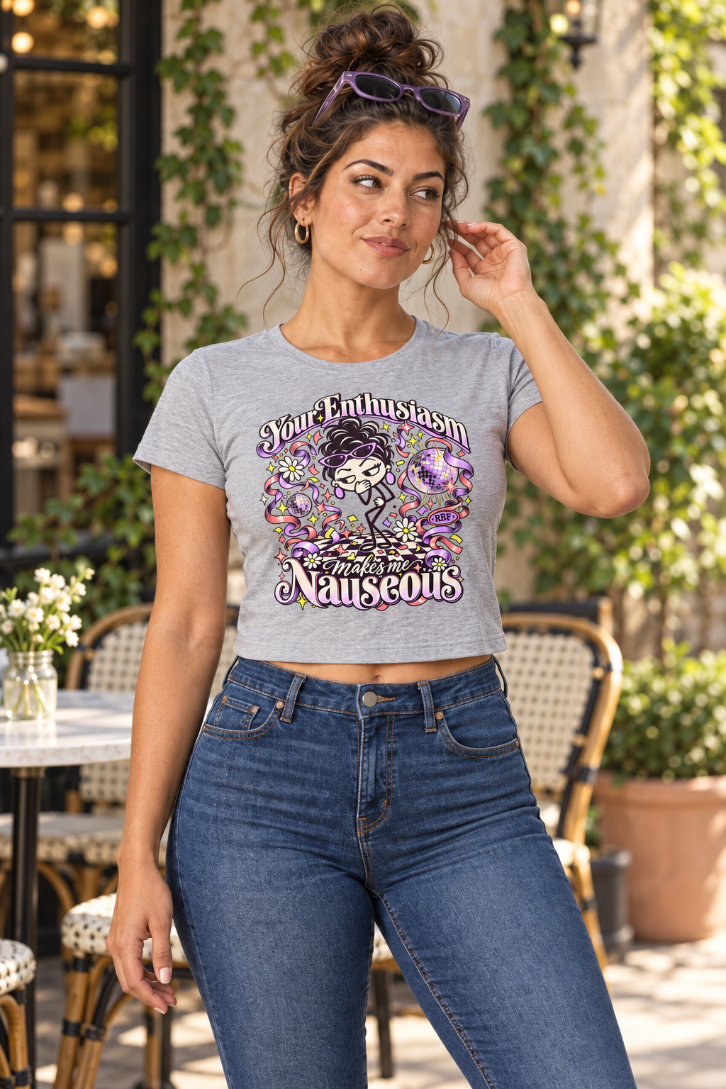 Lifestyle mockup: Your Enthusiasm Makes Me Nauseous crop tee in Athletic Heather. Cafe portrait with the front design visible.
