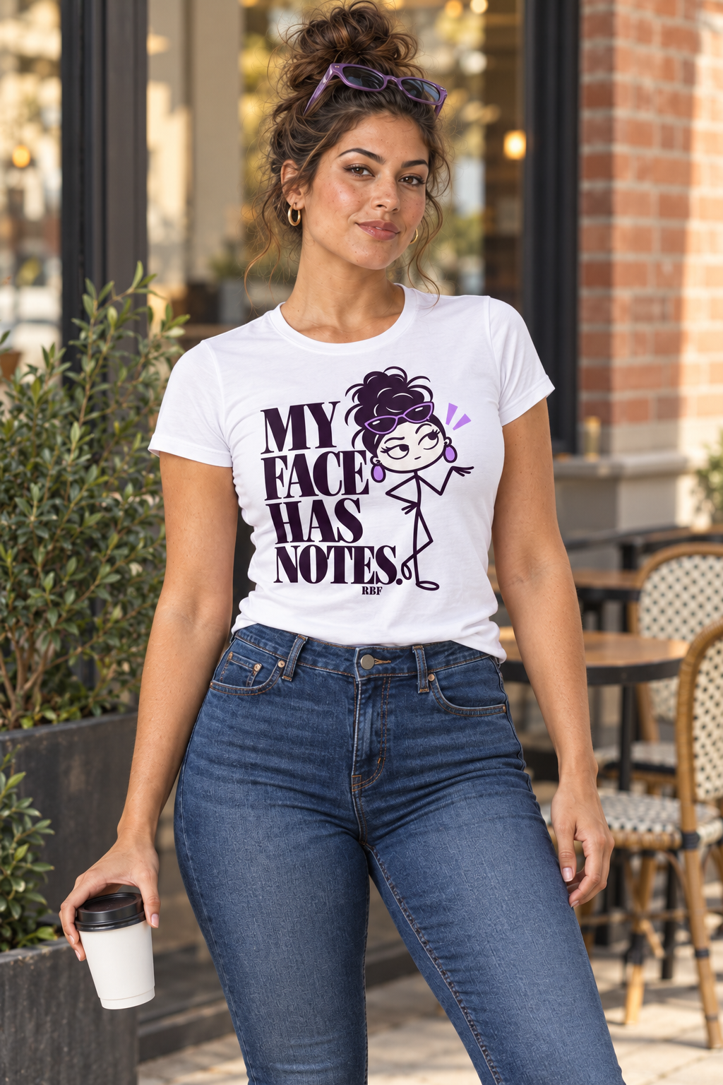 Lifestyle mockup: My Face Has Notes graphic tee in White. Outside a cafe with the front design visible.
